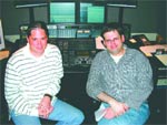 Two men crouched in front of a control console with multiple monitors.