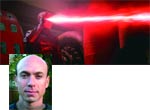 A portrait of a bald man in the bottom left corner against a background of bright red light streaks.