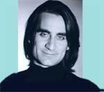 A man with long dark hair and a black turtleneck looking toward the camera.