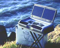 A silver portable electronic device with a screen and keyboard resting on a suitcase near the sea.
