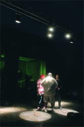 Three people stand in a dark room illuminated by overhead spotlights.