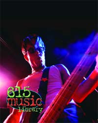 A person playing a bass guitar under blue and red stage lighting.