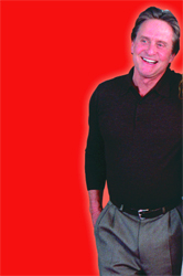 A smiling man wearing a black long-sleeved shirt and grey trousers against a solid red background.