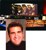 Portrait of a smiling man in a black turtleneck over a background of a television control room with monitors.