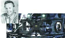 A black and white portrait of a smiling man next to a dark, complex mechanical or industrial object.
