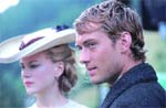 A man with wavy blonde hair and a woman wearing a wide-brimmed hat look off into the distance.