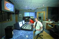 A man in a white shirt sits in a recording studio near a large audio mixing console.