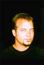 A man with short hair and a small goatee looking toward the camera against a black background.