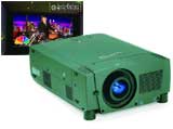 A green digital projector sits in the foreground with a screen displaying a musical performance behind it.