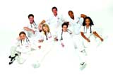 A group of eight diverse medical professionals wearing white scrubs and stethoscopes, posing against a white background.
