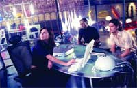 A woman sits at a desk with a computer while two men stand nearby in a dark, modern office.