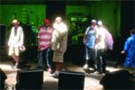 Several people standing on a stage illuminated by green light with speakers in the foreground.