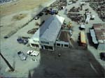 Aerial view of a large white building surrounded by vehicles, equipment, and industrial materials.