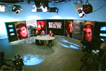 A wide shot of a television studio set featuring a circular table and large portrait banners.
