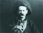 Black and white portrait of a man with a mustache wearing a large hat and a patterned neckerchief.