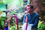 A man in a blue shirt smoking from a pink hookah pipe in a lush, green outdoor setting.