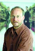 A man with short hair, glasses, and a beard wearing a brown button-down shirt.
