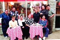 A group of men posing together in front of a storefront with two red and white checkered tables.
