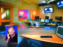 A recording studio with multiple computer monitors, mixing equipment, and an inset of a man talking on a phone.