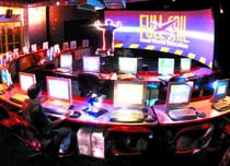 A person sits at a curved desk with several glowing computer monitors in a dark room with a large sign.