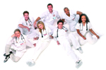 Seven medical professionals in white scrubs and stethoscopes posing together against a white background.