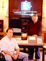 Two men sit and stand in a studio with a large screen displaying the InfiniFilm logo and audio equipment.