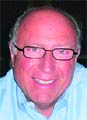 A smiling man with glasses and a light blue shirt.
