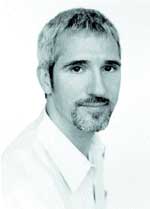 A headshot of a man with short hair and a goatee wearing a white shirt against a white background.