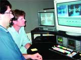 Two people look at computer monitors displaying graphics in a control room.