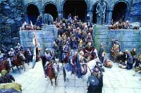 A large crowd of people and mounted riders gathered in a stone courtyard with arched entryways.
