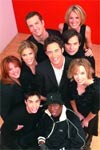 Group of nine smiling people in black clothing posing against a bright red backdrop.