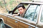 A man leans out of the window of a brown station wagon with wood paneling.