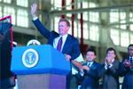 A man in a dark suit and red tie waves his hand while standing behind a blue podium.