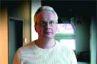 A man with short blonde hair and glasses wearing a light-colored shirt.