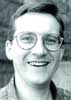 Black and white portrait of a smiling man wearing round-rimmed glasses.