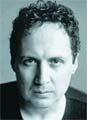 Black and white close-up portrait of a man with curly hair looking directly at the camera.