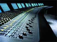 A wide professional audio mixing console with numerous knobs, sliders, and glowing blue display screens.