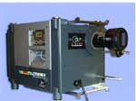A gray rectangular industrial device with a large black lens protruding from the side.