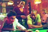 A man leans over a pool table to take a shot while three others watch him in a bar.