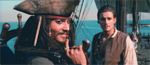 A man in a pirate hat holds a finger to his lips while another man stands behind him on a ship.