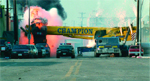 A large yellow sign with 'CHAMPION' text is on fire with thick black and pink smoke behind parked cars.