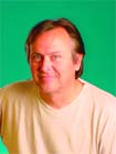 A man with light brown hair wearing a white t-shirt, posing against a solid green background.