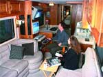 Two people sitting on couches in a wood-paneled RV living area with a television.
