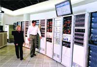 A man and a woman walk past tall rows of server racks in a data center.