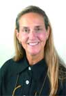A smiling woman with long blonde hair wearing a black collared shirt against a white background.