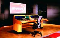 A wooden control console with multiple monitors and an office chair in a dark studio setting.
