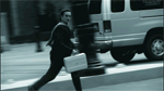 A man in a dark suit runs past a large parked van on a city street.