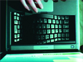 Close-up of hands typing on a dark laptop keyboard under teal lighting.