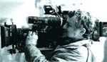 A man looking through the viewfinder of a large professional video camera.