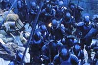 A crowd of people wearing dark armor and helmets in a dimly lit, blue-toned setting.